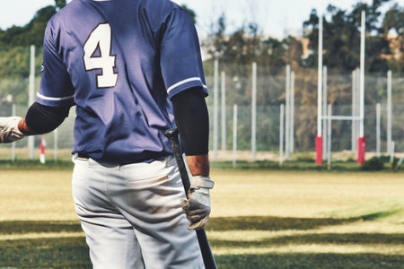 Rear view of a baseball player holding a bat wearing a team uniform on a sports field pitchの写真素材