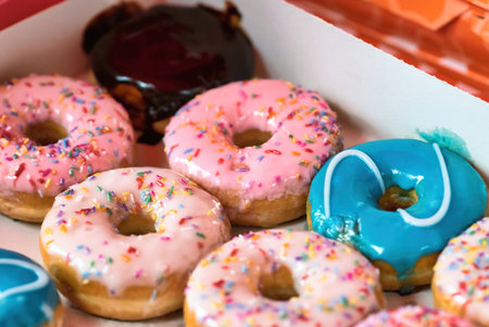 Close-up of a cardboard box full of colorful doughnuts topped with sprinkles and icing sugar coatingの写真素材