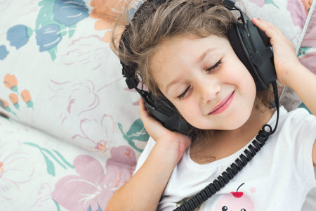 Close-up portrait of a cute white Caucasian girl listening to music with big black plastic headphones, with copyspaceの写真素材