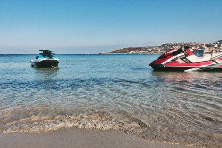 A couple of recreational power jet skis with no people at the water's edge of a sandy beach...