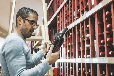 A white Caucasian man holding a red wine bottle, reading the label, in a specialist wine shopの写真素材