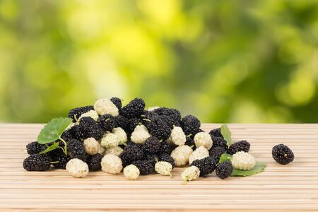 Closeup heap of ripe white and black mulberries with green leaves on table on green leaves background. Horizontalの写真素材