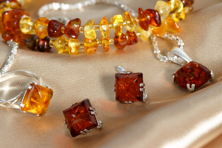 closeup jewerly with  authentic  natural baltic amber : silver earrings, ring and pendant, on brown atlas surface. Bracelet on background. small DOF.の写真素材