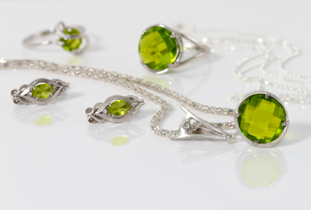 Close-up beauty silver pendant, earrings with peridot on background  chain and rings on white acrylic desk.の写真素材