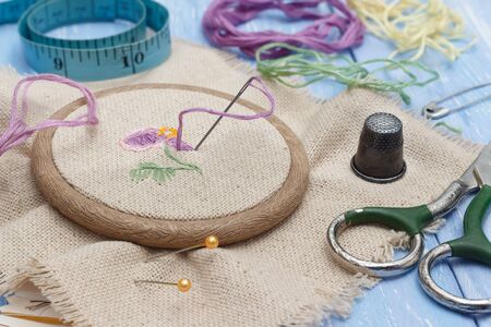 Closeup thread and linen fabric in the wooden embroidery frame for needlework, scissors, thimble and...