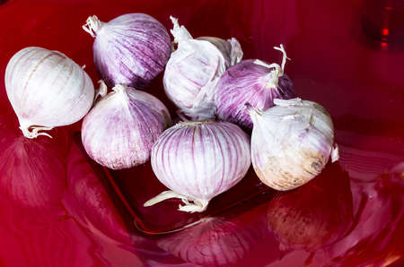 Seven bulbs of garlic lying on a burgundy plate