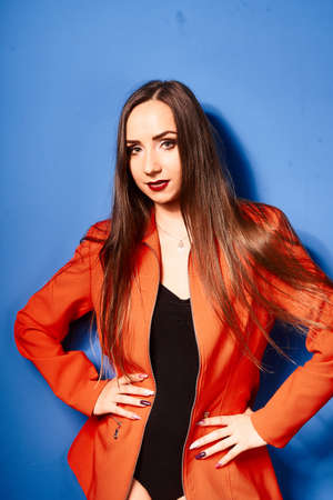 NIce young white girl, wearing black body and orange jacket, blue background, very contrasted...