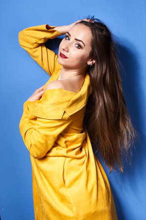 a beautiful girl poses in a yellow coat against a blue wallの写真素材