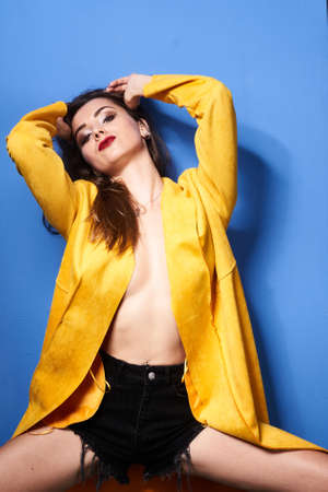 a beautiful girl poses in a yellow coat against a blue wallの写真素材
