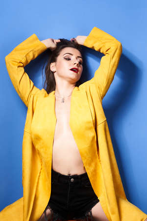 a beautiful girl poses in a yellow coat against a blue wallの写真素材