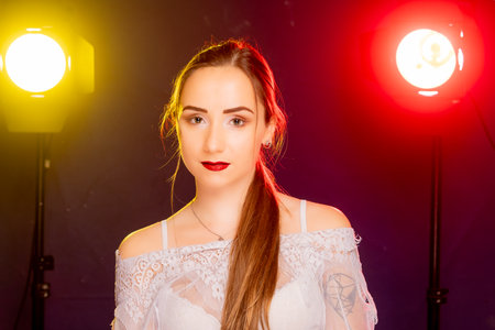 A stunning young European woman strikes a pose in a studio, bathed in a dynamic blend of red and yellow light emanating from behind. The warm hues accentuate her beauty and lend an artistic flair to the image.の写真素材