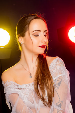 A stunning young European woman strikes a pose in a studio, bathed in a dynamic blend of red and yellow light emanating from behind. The warm hues accentuate her beauty and lend an artistic flair to the image.の写真素材