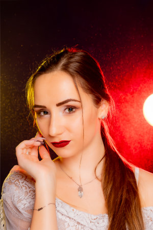 A stunning young European woman strikes a pose in a studio, bathed in a dynamic blend of red and yellow light emanating from behind. The warm hues accentuate her beauty and lend an artistic flair to the image.の写真素材