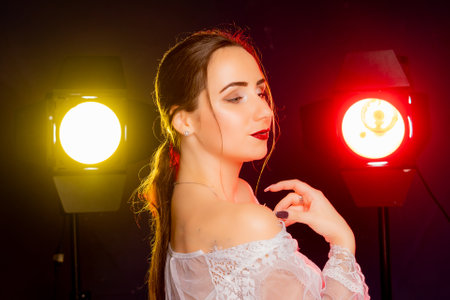 A stunning young European woman strikes a pose in a studio, bathed in a dynamic blend of red and yellow light emanating from behind. The warm hues accentuate her beauty and lend an artistic flair to the image.の写真素材