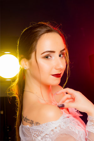A stunning young woman strikes a pose in a studio, bathed in a dynamic blend of red and yellow light emanating from behind. The warm hues accentuate her beauty and lend an artistic flair to the image.の写真素材