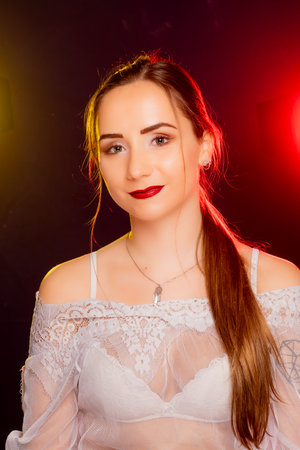 A stunning young European woman strikes a pose in a studio, bathed in a dynamic blend of red and yellow light emanating from behind. The warm hues accentuate her beauty and lend an artistic flair to the image.の写真素材