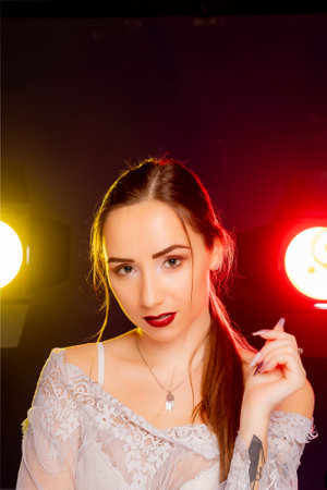 A stunning young woman strikes a pose in a studio, bathed in a dynamic blend of red and yellow light emanating from behind. The warm hues accentuate her beauty and lend an artistic flair to the image.の写真素材