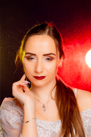 A young woman strikes a pose in a studio, bathed in a dynamic blend of red and yellow light emanating from behind. The warm hues accentuate her beauty and lend an artistic flair to the image.の写真素材