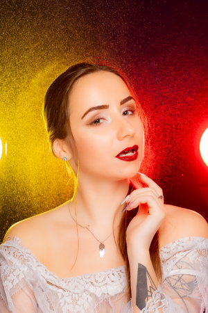 A stunning young European woman strikes a pose in a studio, bathed in a dynamic blend of red and yellow light emanating from behind. The warm hues accentuate her beauty and lend an artistic flair to the image.の写真素材