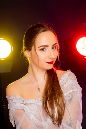 A stunning young European woman strikes a pose in a studio, bathed in a dynamic blend of red and yellow light emanating from behind. The warm hues accentuate her beauty and lend an artistic flair to the image.の写真素材
