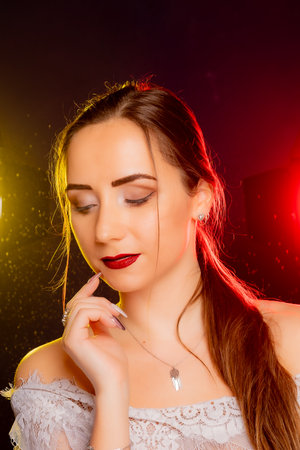 A stunning young European woman strikes a pose in a studio, bathed in a dynamic blend of red and yellow light emanating from behind. The warm hues accentuate her beauty and lend an artistic flair to the image.の写真素材