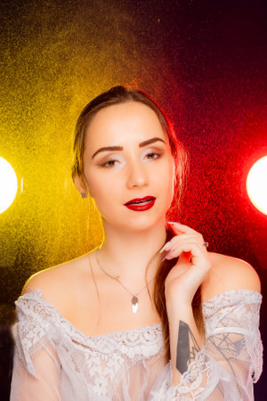 A stunning young woman strikes a pose in a studio, bathed in a dynamic blend of red and yellow light emanating from behind. The warm hues accentuate her beauty and lend an artistic flair to the image.の写真素材
