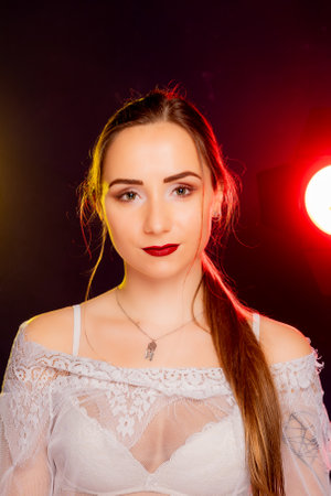 A stunning young woman strikes a pose in a studio, bathed in a dynamic blend of red and yellow light emanating from behind. The warm hues accentuate her beauty and lend an artistic flair to the image.の写真素材