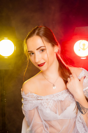 A stunning young European woman strikes a pose in a studio, bathed in a dynamic blend of red and yellow light emanating from behind. The warm hues accentuate her beauty and lend an artistic flair to the image.の写真素材