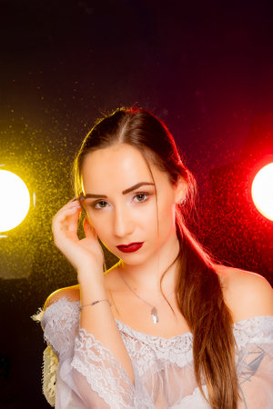 A stunning young European woman strikes a pose in a studio, bathed in a dynamic blend of red and yellow light emanating from behind. The warm hues accentuate her beauty and lend an artistic flair to the image.の写真素材