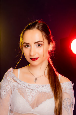 A stunning young European woman strikes a pose in a studio, bathed in a dynamic blend of red and yellow light emanating from behind. The warm hues accentuate her beauty and lend an artistic flair to the image.の写真素材