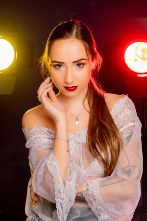 A stunning young European woman strikes a pose in a studio, bathed in a dynamic blend of red and yellow light emanating from behind. The warm hues accentuate her beauty and lend an artistic flair to the image.の写真素材