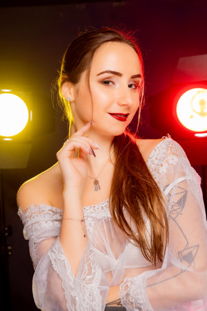 A stunning young woman strikes a pose in a studio, bathed in a dynamic blend of red and yellow light emanating from behind. The warm hues accentuate her beauty and lend an artistic flair to the image.の写真素材