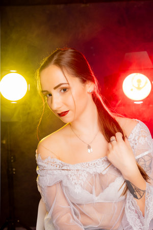 A stunning young woman strikes a pose in a studio, bathed in a dynamic blend of red and yellow light emanating from behind. The warm hues accentuate her beauty and lend an artistic flair to the image.の写真素材