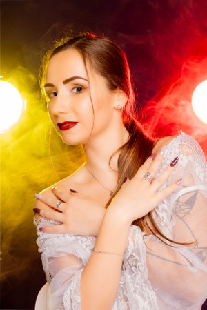 A stunning young European woman strikes a pose in a studio, bathed in a dynamic blend of red and yellow light emanating from behind. The warm hues accentuate her beauty and lend an artistic flair to the image.の写真素材