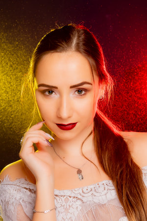 A stunning young European woman strikes a pose in a studio, bathed in a dynamic blend of red and yellow light emanating from behind. The warm hues accentuate her beauty and lend an artistic flair to the image.の写真素材