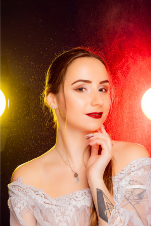 A stunning young European woman strikes a pose in a studio, bathed in a dynamic blend of red and yellow light emanating from behind. The warm hues accentuate her beauty and lend an artistic flair to the image.の写真素材