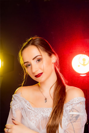 A stunning young European woman strikes a pose in a studio, bathed in a dynamic blend of red and yellow light emanating from behind. The warm hues accentuate her beauty and lend an artistic flair to the image.の写真素材