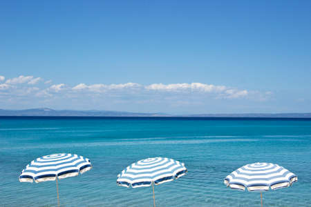 Three umbrellas over the blue sea waterの写真素材