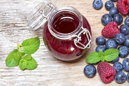 Raspberry marmalade and the fresh raspberries and blueberries on a wooden background