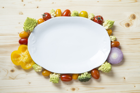 Fresh vegetables with a white plate on wooden tableの写真素材