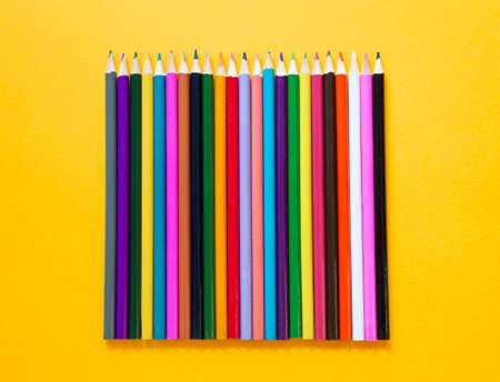 Colored wooden pencils on yellow background