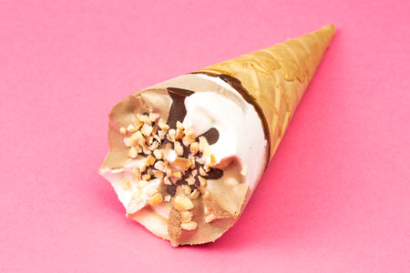 Chocolate and vanilla ice cream in a waffle cone on pink background