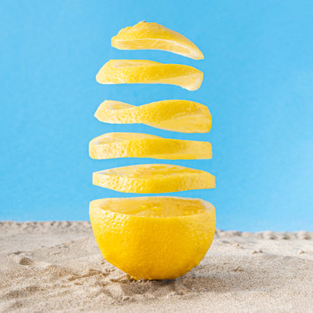 Lemon on a beach sand. Slices floating in the air against pastel blue background. Summer nature, minimal concept.の写真素材