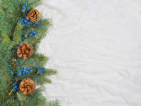 Christmas card with copy space made of natural Christmas tree branches, cones and blue berries, against white natural silk background. Minimal New Year concept. Fla tlay composition.の写真素材