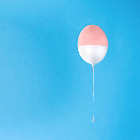 Levitating Easter egg with liquid white paint dripping, against blue background with copy space. Minimal Easter concept. Abstract painted egg.の写真素材