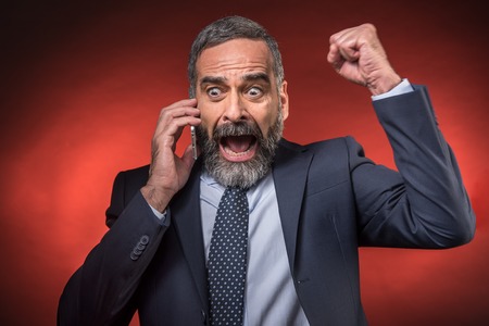 Cheering businessman receiving great news over his phone, red backgroundの写真素材