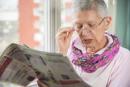 Senior elderly lady having troubles with her eye glasses, cant see well and cant read the small letters in the newspapersの写真素材