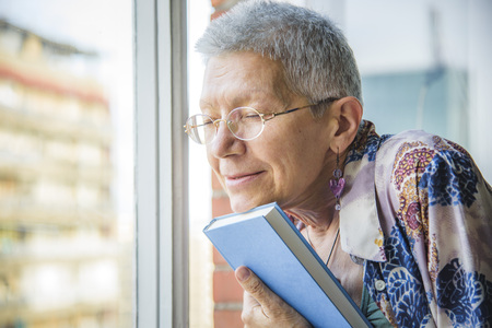 Senior woman holding her favorite book, remembering old loveの写真素材