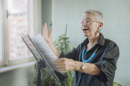 Senior woman practicing her singing skills from a stack of musical sheetsの写真素材