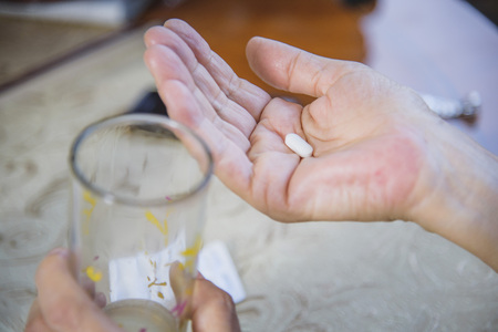 Closeup of senior ladys hands holding a pill and a glass of waterの写真素材